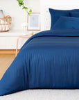 Blue bedding set on a bed in a bedroom with a white wall and wooden floor.