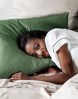 Woman lying in bed with olive green pillow and sand beige bedding