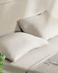 Neatly made bed with beige pillows and sheets, accompanied by a small plant.