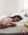 Woman sleeping peacefully in a bed with white bedding and a vase of flowers on the nightstand.