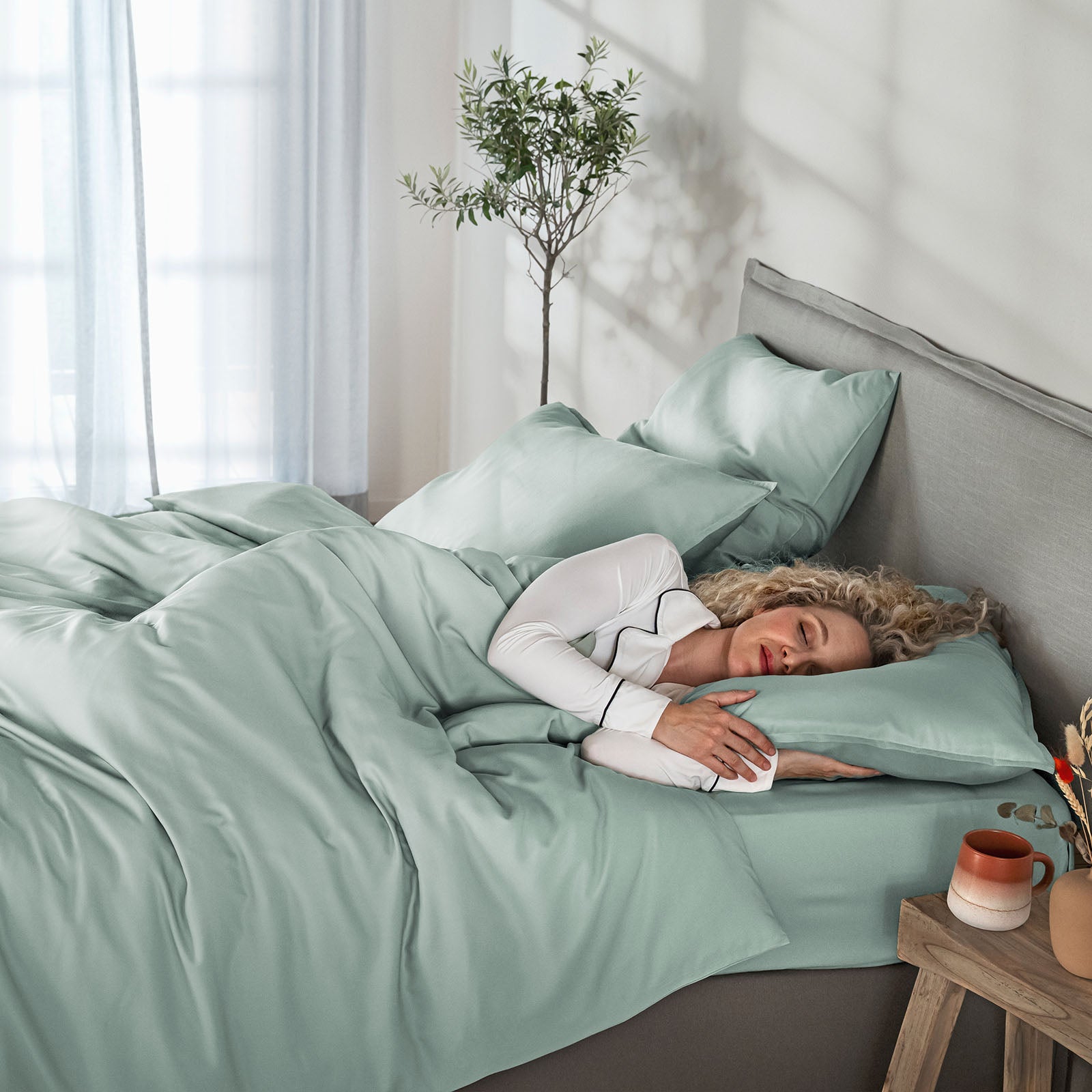Woman lying in bed with light green bedding in a bright bedroom.