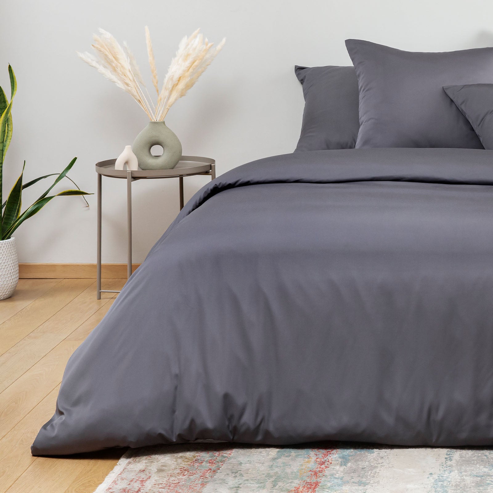 Gray bedding set on a bed with a side table and decorative items in a room.