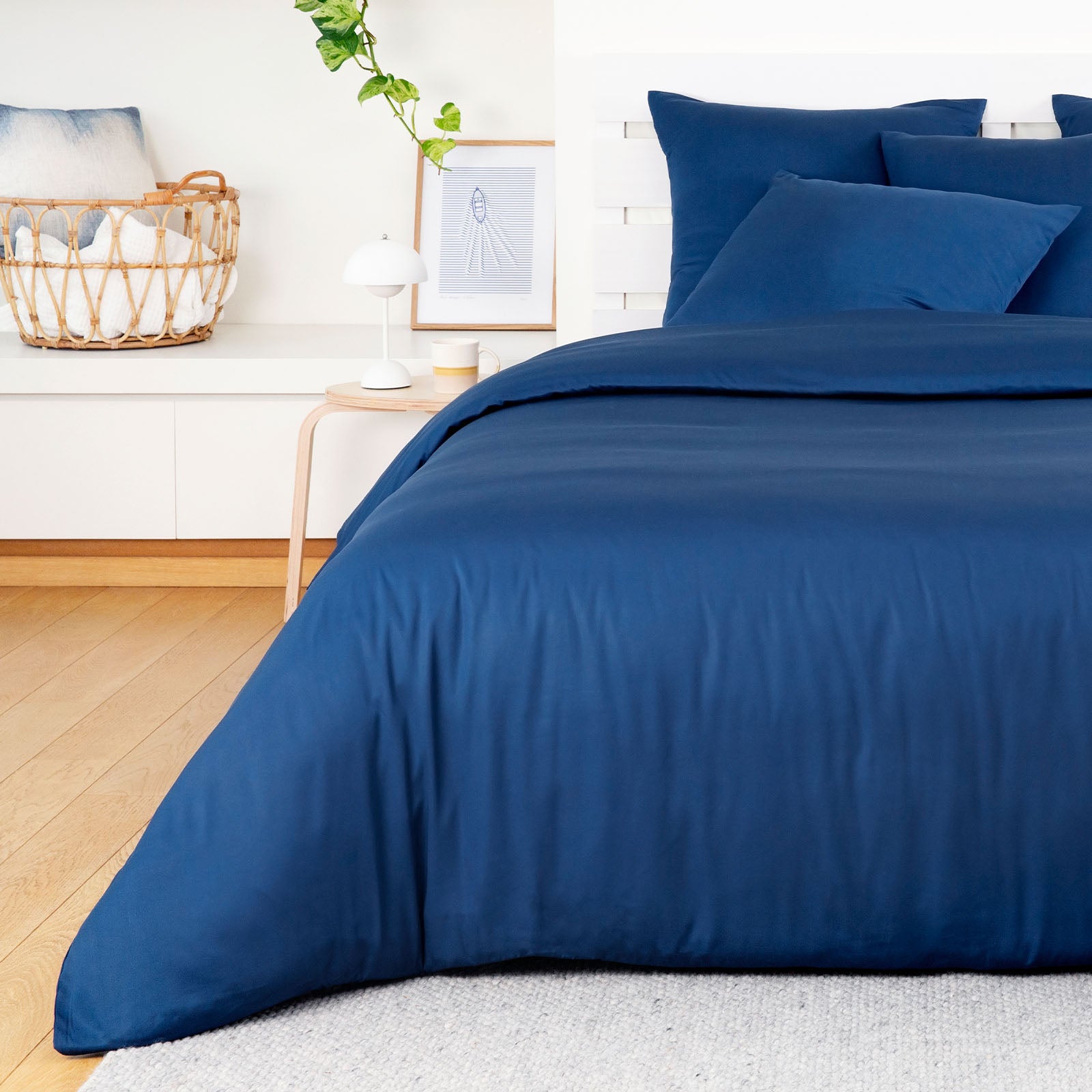 Blue bedding set on a bed in a bedroom with a white wall and wooden floor.