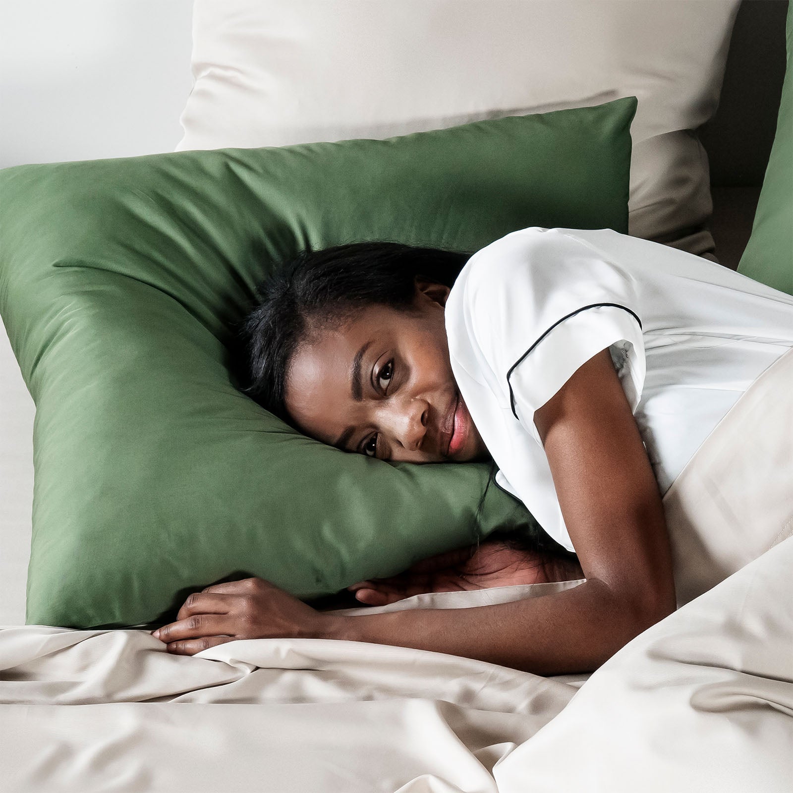 Woman lying in bed with olive green pillow and sand beige bedding