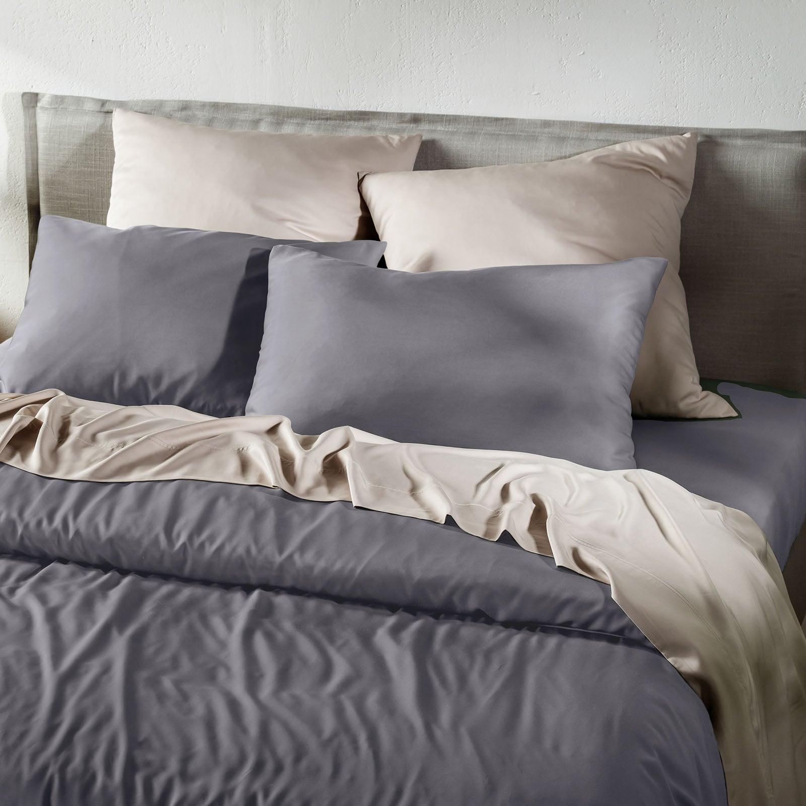 Gray bedding set with pillows on a bed against a white wall