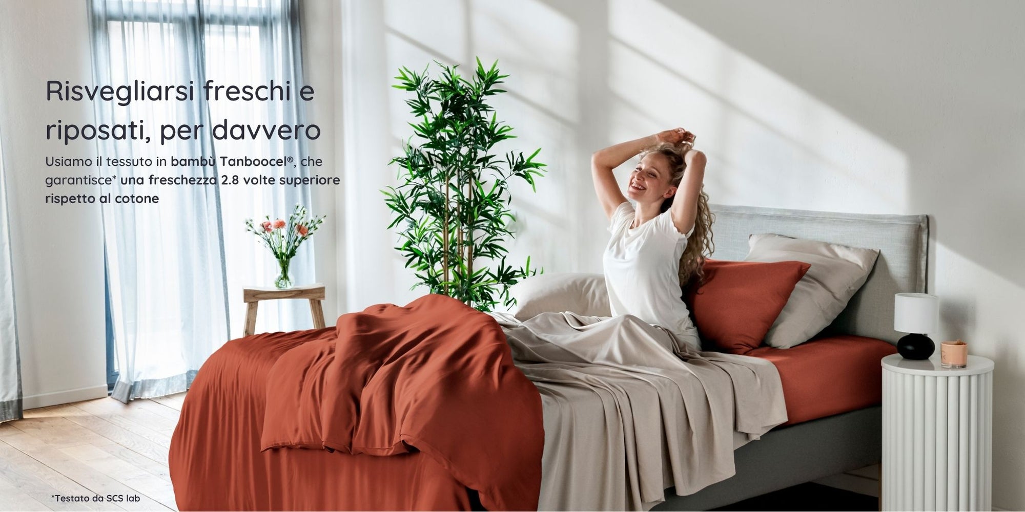 Woman waking up in a bright bedroom in a bed with bambaw cozy bamboo bedsheets in terraccota and sand colours with natural light and plants.