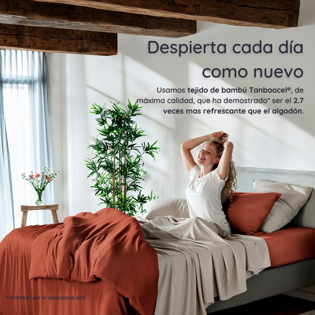 Mujer despertándose en un dormitorio luminoso con ropa de cama de bambú terracota de Bambaw y paredes blancas.